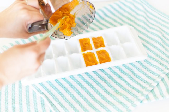 Pouring baby food in to the ice cube tray to freeze